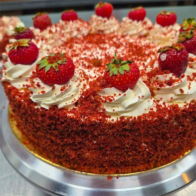 Tort red velvet z kremem i truskawkami, obsypany czerwoną kruszonką biszkoptową